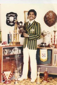Norm Stevens in Olympic uniform, holding trophy, is front of collection of other trophies