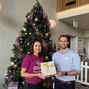 Simone Garske and Geoff Grima standing in front of the ground floor Christmas tree holding a present