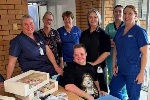 Former CKW patient Corey seated surrounded by mum and staff