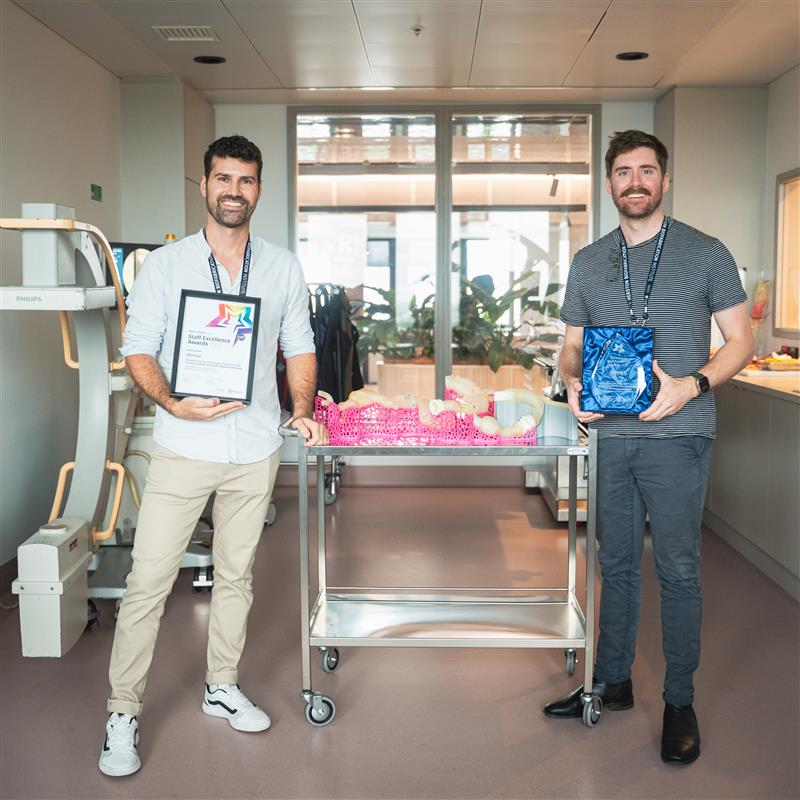 Two men holding awards and standing either side of a trolley