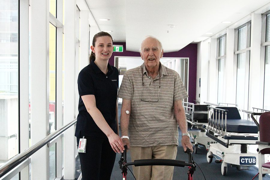 Man with walker supervised by physiotherapist