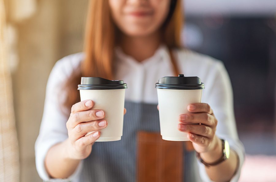 A waitress holding and serving two paper cups of hot coffee in cafe