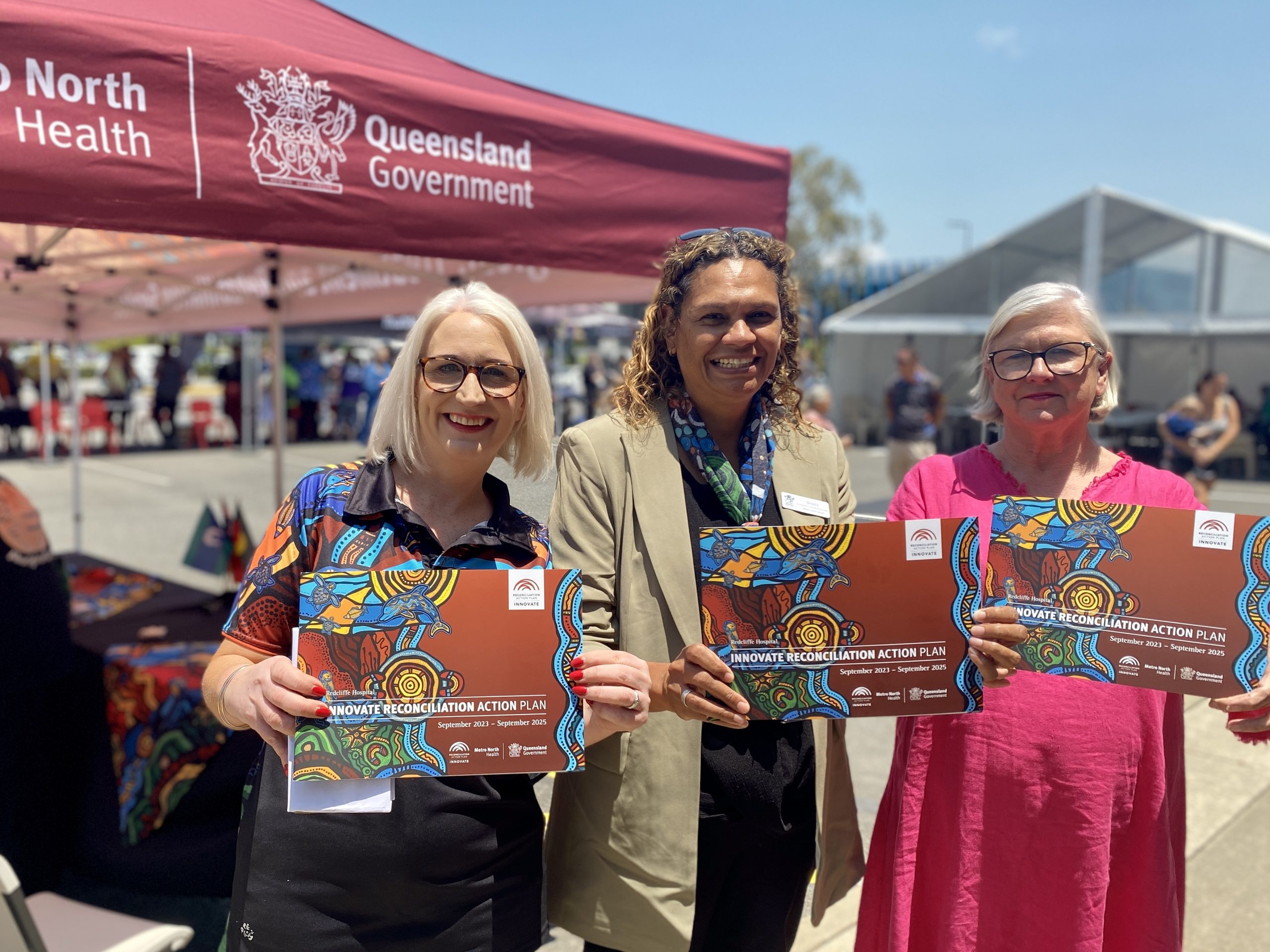 Three women hold copies of the Redcliffe Hospital Reconciliation Action Plan