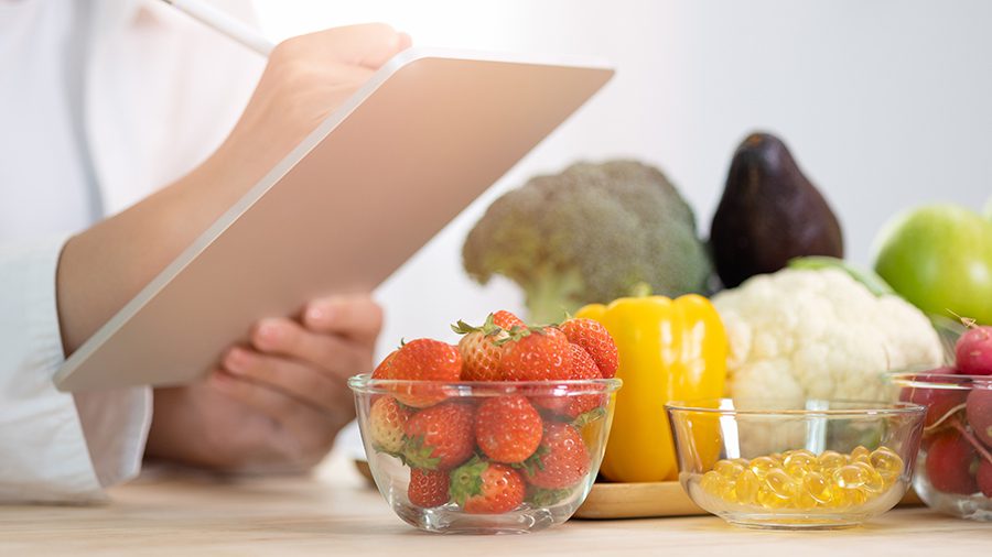 Person holding a digital tablet surrounded by a variety of fresh fruits and vegetables.